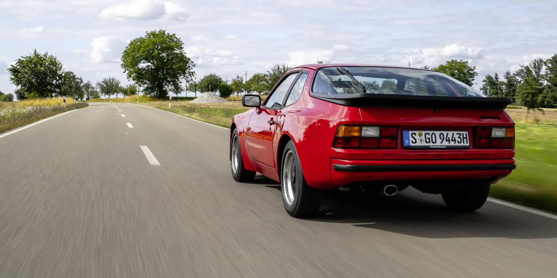 Czerwone Porsche 944 w ruchu na pustej drodze, widok z tyłu