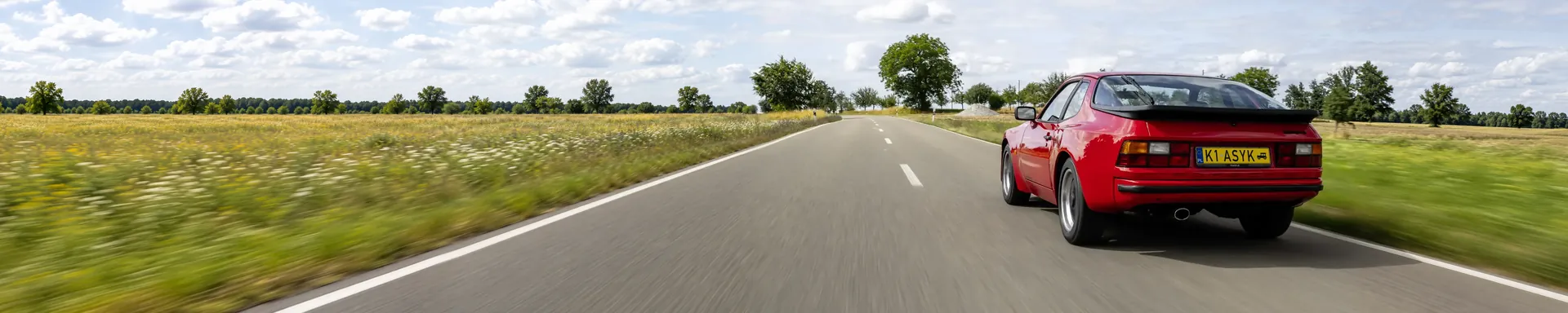 Czerwone Porsche 944 w ruchu na pustej drodze, widok z tyłu