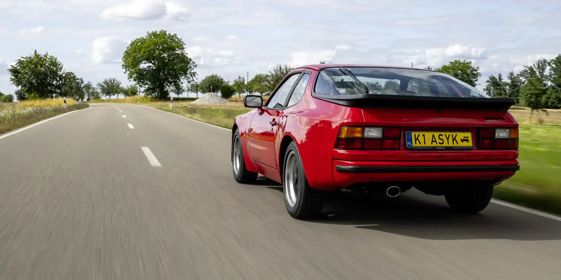 Czerwone Porsche 944 w ruchu na pustej drodze, widok z tyłu