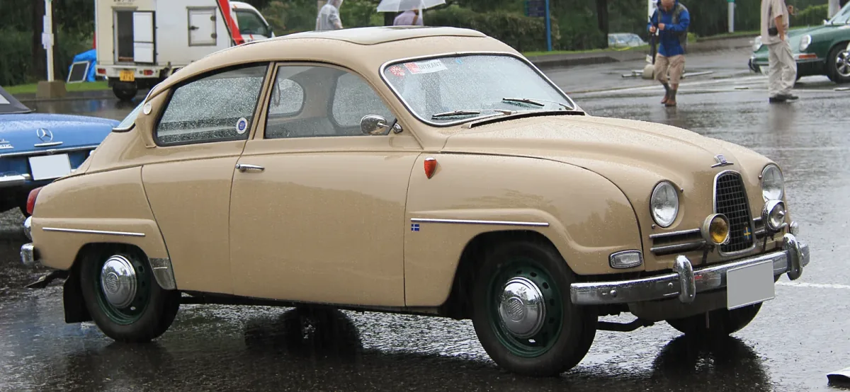Beżowy Saab 96 z 1961 roku na placu podczas zlotu klasyków — ujęcie trzy czwarte z przodu.