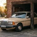 Beżowy Mercedes W123 w progu garażu — pół w słońcu, pół w cieniu. Decyzja o żółtych tablicach wygląda dokładnie tak.
