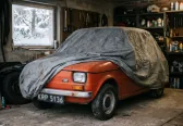 Fiat 126p pod pokrowcem w domowym garażu, za oknem śnieg. Sezon skończony — a OC wciąż tyka, chyba że wybrałeś polisę krótkoterminową.