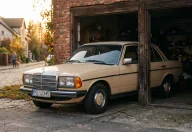Beżowy Mercedes W123 w progu garażu — pół w słońcu, pół w cieniu. Decyzja o żółtych tablicach wygląda dokładnie tak.
