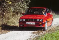 Czerwone E30 na szutrowej drodze, w materiałach prasowych BMW. Egzemplarz w takim stanie trafia dziś do ogłoszeń rzadko, a jego cena zaczyna się tam, gdzie inne się kończą.