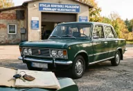 Zielony Fiat 125p przed stacją kontroli pojazdów — na błotniku karta pojazdu i kluczyki. Rachunek za żółte tablice zaczyna się jeszcze przed badaniem.