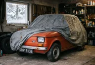 Fiat 126p pod pokrowcem w domowym garażu, za oknem śnieg. Sezon skończony — a OC wciąż tyka, chyba że wybrałeś polisę krótkoterminową.