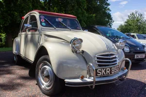 Kremowy Citroën 2CV z 1968 roku z bordowym dachem na zlocie klasyków — ujęcie trzy czwarte z przodu.