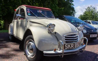 Kremowy Citroën 2CV z 1968 roku z bordowym dachem na zlocie klasyków — ujęcie trzy czwarte z przodu.