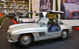 Kadru nie da się pomylić z żadnym innym autem — 300 SL Coupé ze wzniesionymi skrzydłami i kraciastą tapicerką. Drzwi w dachu nie były fanaberią stylisty: wymusiła je wysoka rama przestrzenna, przez którą inaczej nie dało się wsiąść.