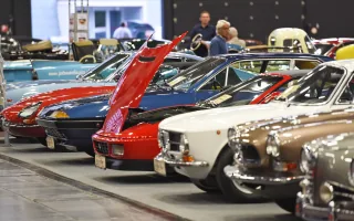 Rząd klasycznych samochodów na targach w hali wystawowej — widoczne m.in. Fiat Dino Coupé, Volvo P1800 i inne europejskie klasyki lat sześćdziesiątych i siedemdziesiątych