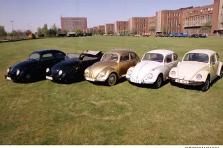 Pięć historycznych Volkswagenów Garbusów w rzędzie na trawie przed fabryką w Wolfsburgu — roczniki od 1938 do 1976.