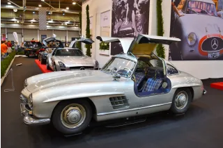 Kadru nie da się pomylić z żadnym innym autem — 300 SL Coupé ze wzniesionymi skrzydłami i kraciastą tapicerką. Drzwi w dachu nie były fanaberią stylisty: wymusiła je wysoka rama przestrzenna, przez którą inaczej nie dało się wsiąść.