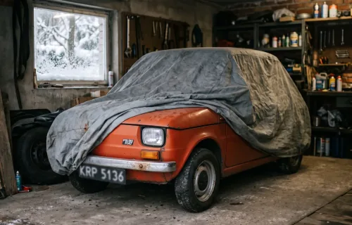 Fiat 126p pod pokrowcem w domowym garażu, za oknem śnieg. Sezon skończony — a OC wciąż tyka, chyba że wybrałeś polisę krótkoterminową.