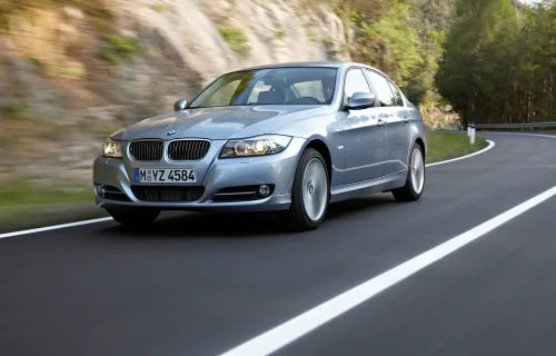 Srebrne BMW E90 na krętej drodze, widok z przodu pod kątem.