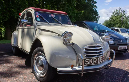 Kremowy Citroën 2CV z 1968 roku z bordowym dachem na zlocie klasyków — ujęcie trzy czwarte z przodu.