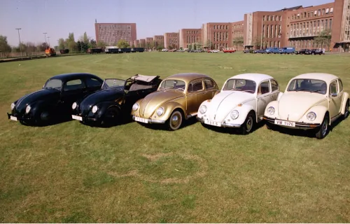 Pięć historycznych Volkswagenów Garbusów w rzędzie na trawie przed fabryką w Wolfsburgu — roczniki od 1938 do 1976.