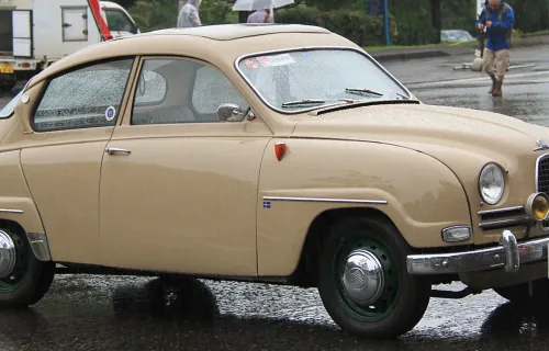 Beżowy Saab 96 z 1961 roku na placu podczas zlotu klasyków — ujęcie trzy czwarte z przodu.