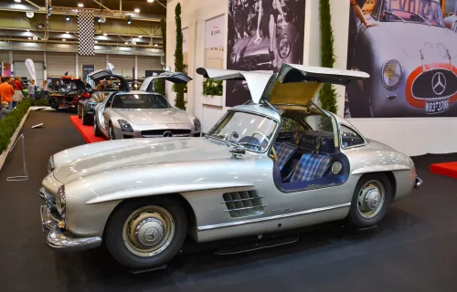 Kadru nie da się pomylić z żadnym innym autem — 300 SL Coupé ze wzniesionymi skrzydłami i kraciastą tapicerką. Drzwi w dachu nie były fanaberią stylisty: wymusiła je wysoka rama przestrzenna, przez którą inaczej nie dało się wsiąść.