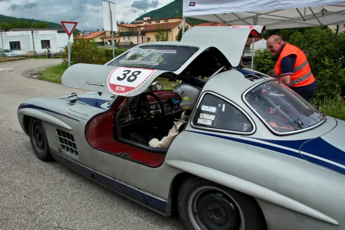 Skrzydlak wciąż jeździ — 300 SL Coupé z podniesionym skrzydłem na trasie rajdu klasyków. Po siedmiu dekadach ten kształt: płaska maska, długi przód i dach spływający do krótkiego tyłu, nie zestarzał się ani trochę.