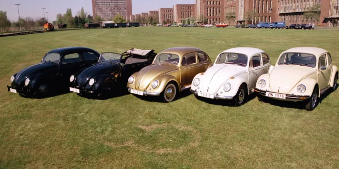Pięć historycznych Volkswagenów Garbusów w rzędzie na trawie przed fabryką w Wolfsburgu — roczniki od 1938 do 1976.