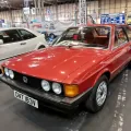 Odrestaurowany Volkswagen Scirocco I 1.6 z 1980 roku w czerwonym lakierze — przód z lewej strony, cztery okrągłe reflektory i czarna atrapa ze znaczkiem VW. Zdjęcie z wystawy NEC Restoration Show w Birmingham, marzec 2022.
