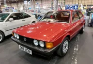 Odrestaurowany Volkswagen Scirocco I 1.6 z 1980 roku w czerwonym lakierze — przód z lewej strony, cztery okrągłe reflektory i czarna atrapa ze znaczkiem VW. Zdjęcie z wystawy NEC Restoration Show w Birmingham, marzec 2022.