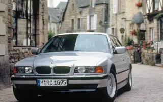 Srebrny BMW 740i na brukowanej uliczce francuskiego miasteczka — nadwozie w krótszym rozstawie osi, przed liftingiem z 1998 roku