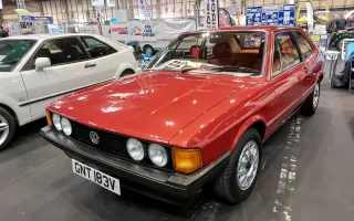 Odrestaurowany Volkswagen Scirocco I 1.6 z 1980 roku w czerwonym lakierze — przód z lewej strony, cztery okrągłe reflektory i czarna atrapa ze znaczkiem VW. Zdjęcie z wystawy NEC Restoration Show w Birmingham, marzec 2022.