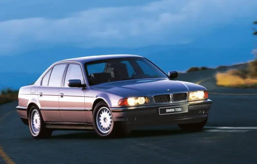 BMW 735i na górskiej drodze o zmierzchu. Ta powściągliwa bryła, ganiona w połowie lat dziewięćdziesiątych za brak prezencji, dziś czyta się jako klasa