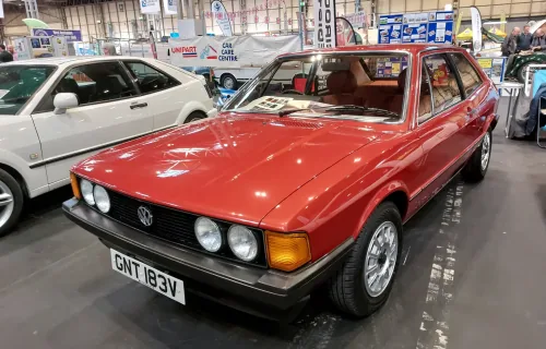 Odrestaurowany Volkswagen Scirocco I 1.6 z 1980 roku w czerwonym lakierze — przód z lewej strony, cztery okrągłe reflektory i czarna atrapa ze znaczkiem VW. Zdjęcie z wystawy NEC Restoration Show w Birmingham, marzec 2022.